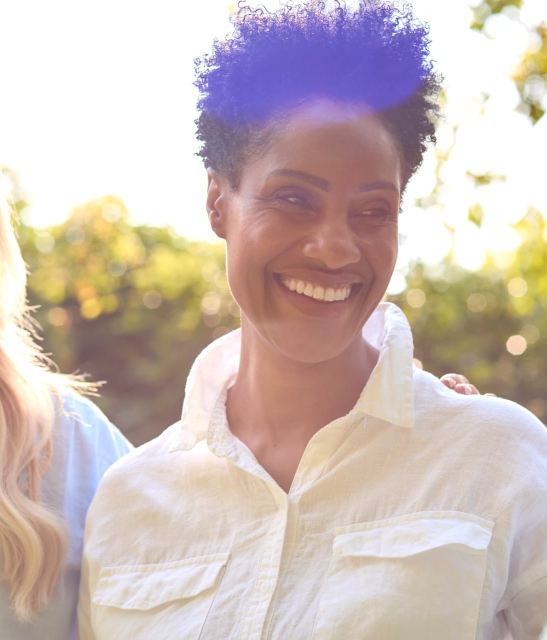 Three women smiling together outdoors in warm sunlight